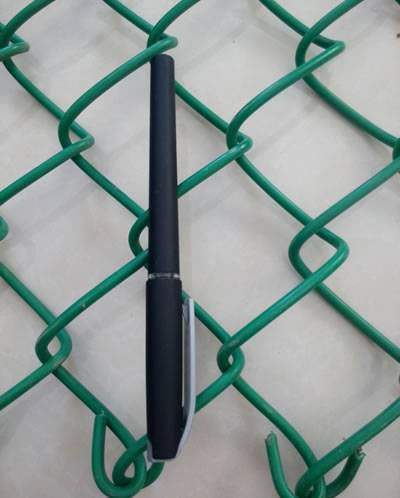 Una penna nera è disposta sul PVC verde ha ricoperto il recinto del collegamento a catena e la lunghezza di due fori è equivalente con la lunghezza di una penna.